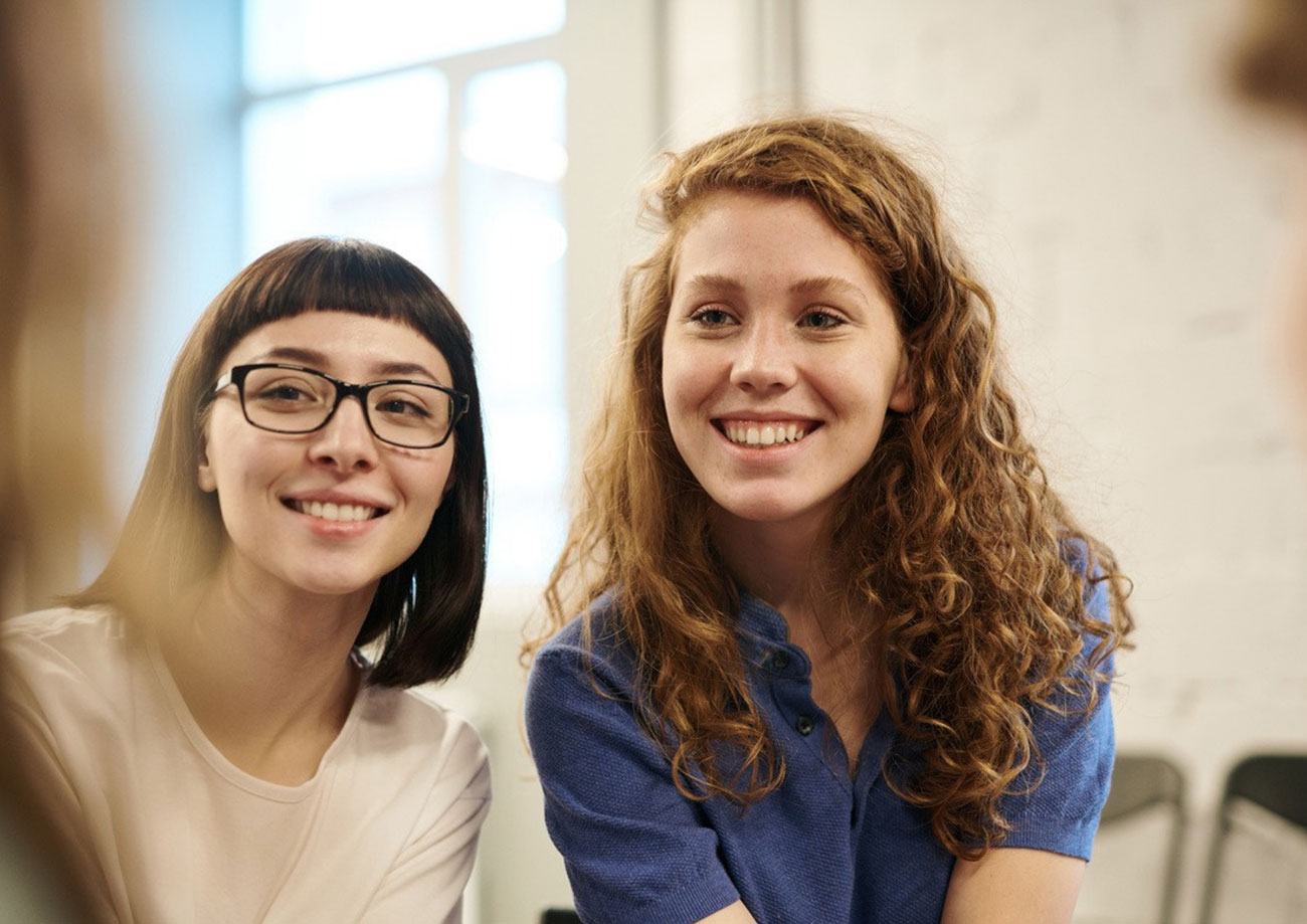Two young people, one with glasses, looking at something together and smiling